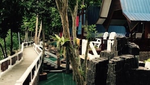 A bridge over a pool with a rustic wooden structure and a building with a blue roof in the background. - Shari-La Island Resort (Pulau Perhentian Kecil)