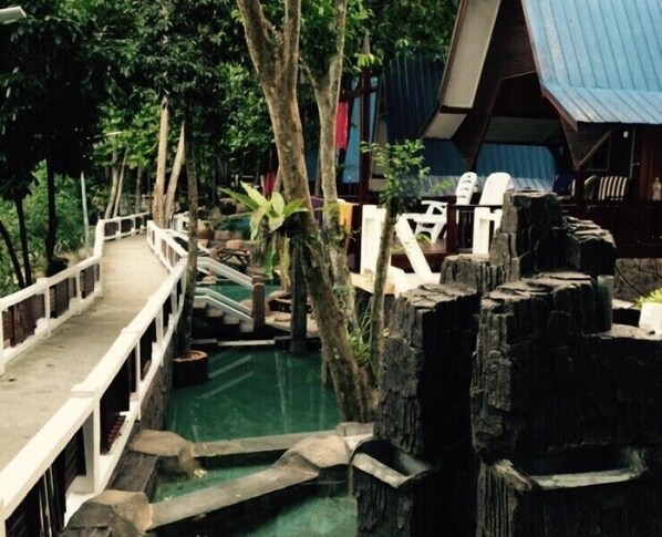 A bridge over a pool with a rustic wooden structure and a building with a blue roof in the background. - Shari-La Island Resort (Pulau Perhentian Kecil)