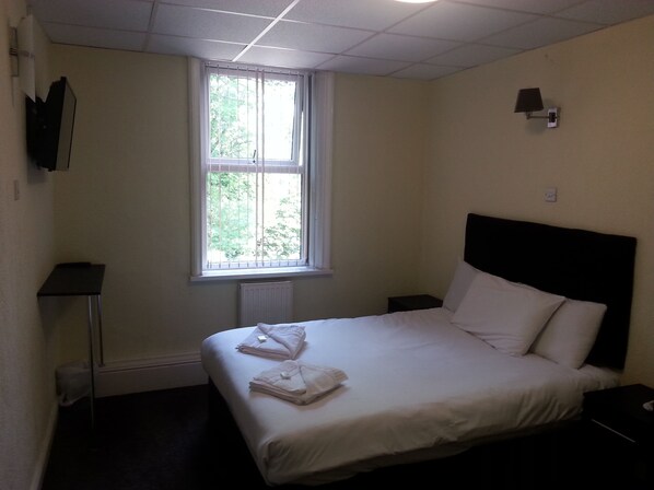 A hotel room with a bed, a window, a nightstand, and a wall-mounted lamp. - The Park Hotel (Bradford)