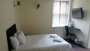 A neatly made bed with white linens and pillows, a desk with a chair, a television mounted on the wall, and a window with curtains. - The Park Hotel (Bradford)