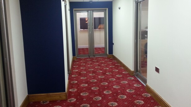 A hallway with a red patterned carpet, blue walls, and a door leading to another room. - The Park Hotel (Bradford)
