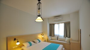 A hotel room with a bed, bedside tables, a window with curtains, an air conditioning unit, and a wall-mounted light fixture. - Golkoy Suites Boutique Hotel (Bodrum)