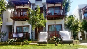 A two-story building with balconies, a small garden area with chairs, and a pathway leading to the entrance. - Golkoy Suites Boutique Hotel (Bodrum)