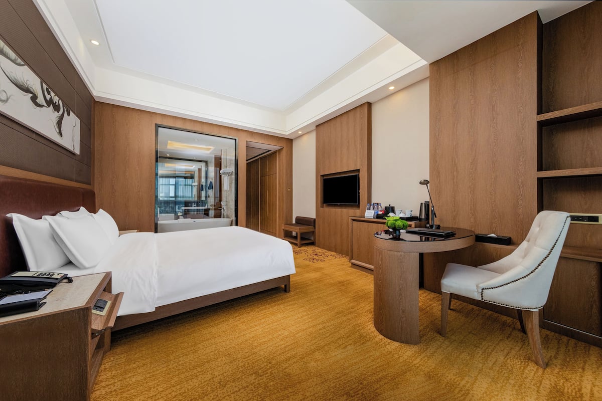 Habitación de hotel con una cama grande, un escritorio con silla, un televisor y un panel de pared de madera.