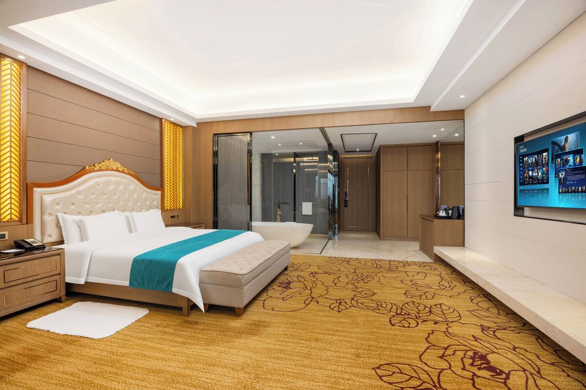 Una habitación de hotel moderna con una cama grande, una zona de estar, un baño y un televisor en la pared.