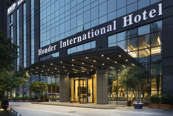 The exterior of the Honder International Hotel with a glass facade, a covered entrance, and a well-lit lobby area. - Honder International Hotel (Guangzhou)