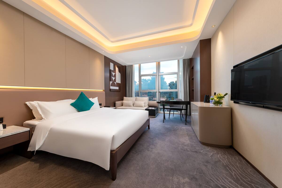 Habitación de hotel moderna con una cama grande, un escritorio, un televisor y vistas de la ciudad.