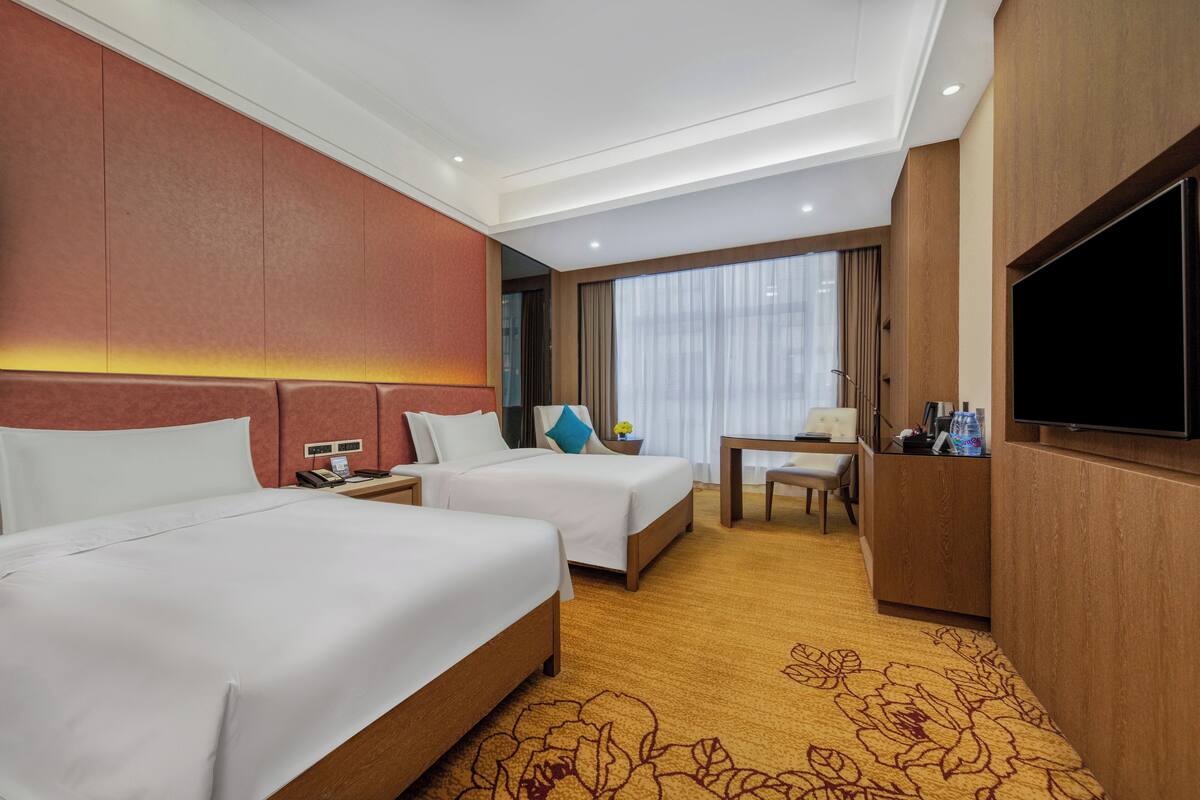 Una habitación de hotel con dos camas, un escritorio, un televisor y un ventanal con cortinas.