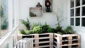 A corner with wooden crates used as planters, a wreath on the wall, and a window with blinds.