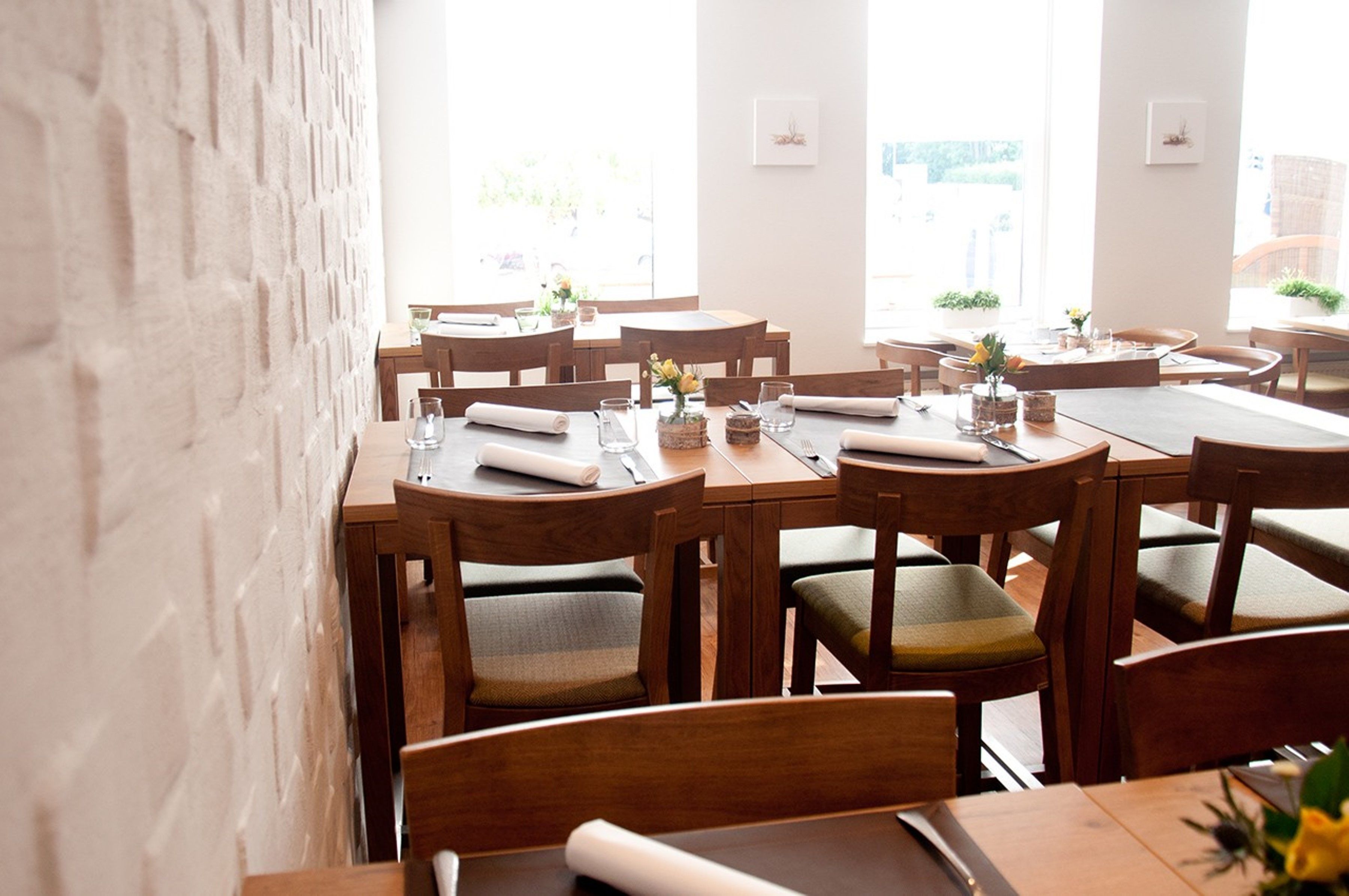 Un restaurante con mesas y sillas de madera, ordenado con servilletas y cubiertos.