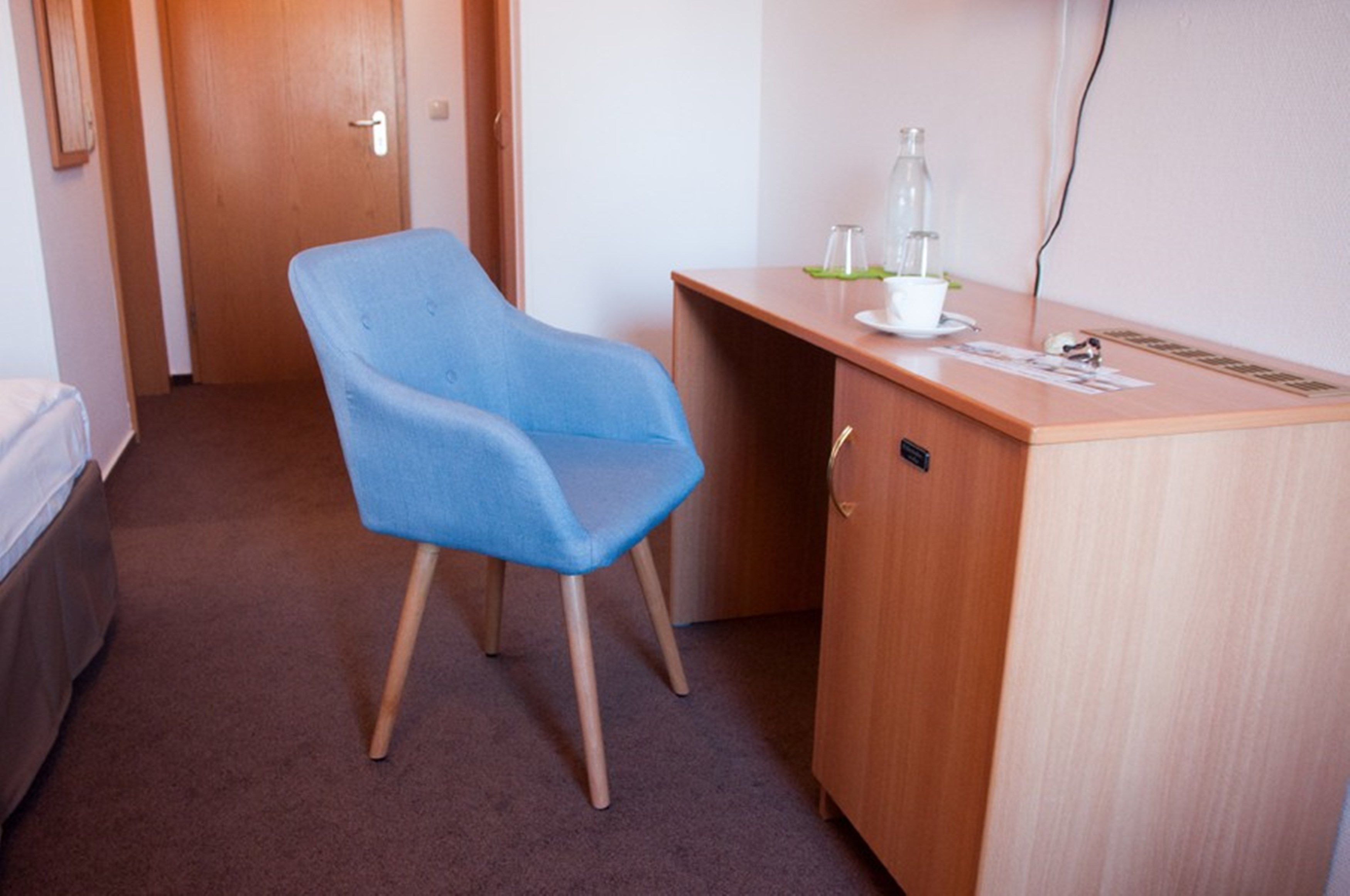 A small room with a blue chair, a wooden desk, and a bed.