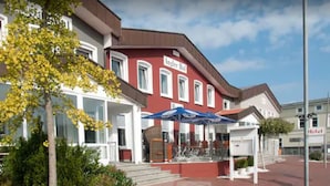 A hotel with a red facade, white windows, and a covered outdoor seating area.