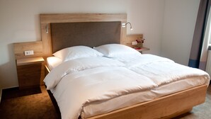 A large bed with a wooden headboard, a bedside table with a lamp, and a nightstand with a vase of flowers.