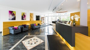 Een moderne hotellobby met een receptiebalie, banken en kunstwerken aan de muur.