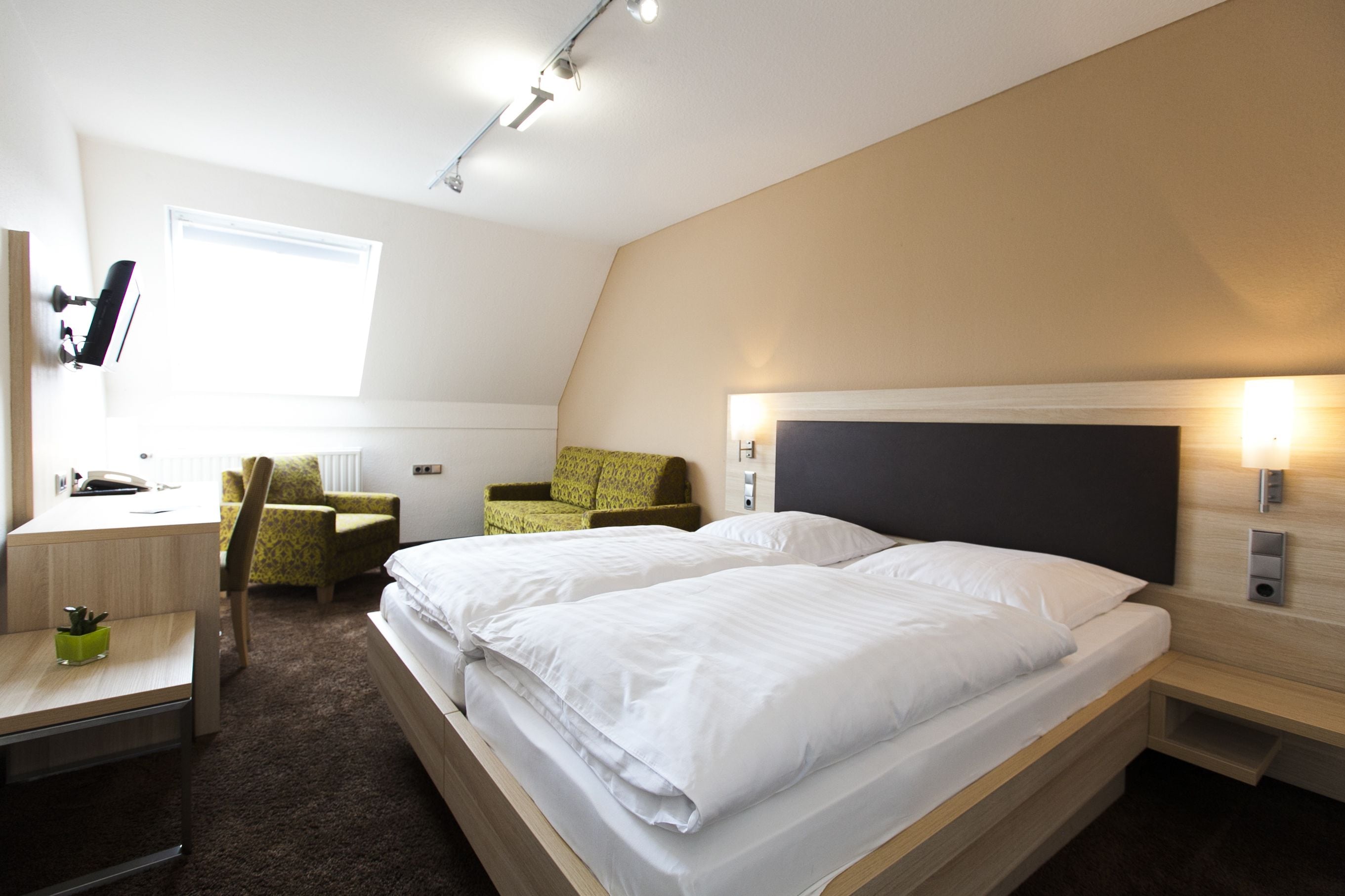 A modern hotel room with a large bed, a desk, a chair, and a small seating area.