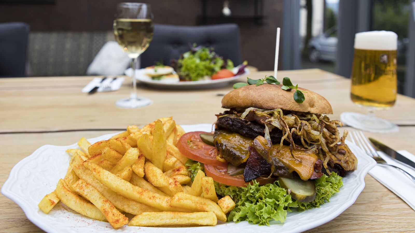 Ein Teller mit Essen, darunter Pommes, ein Burger und ein Glas Bier, auf einer Holztisch.