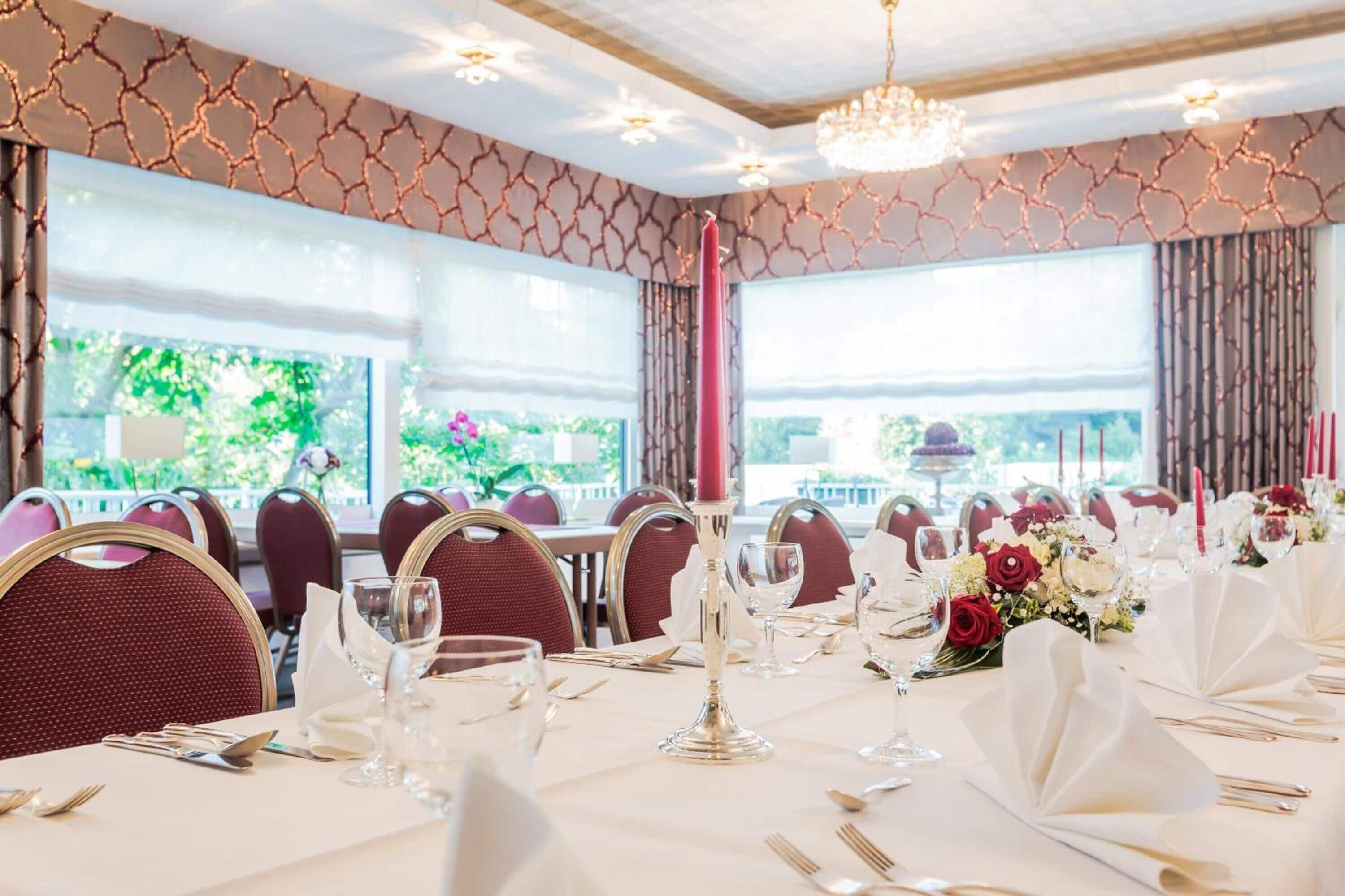 A dining area with tables set for a formal event, featuring chandeliers and large windows with a view.