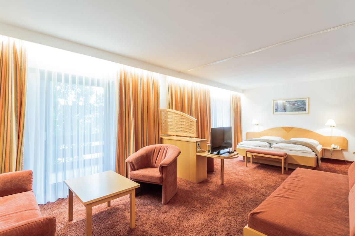 Habitación de hotel con cama, escritorio con computadora, silla, sofá y cortinas.