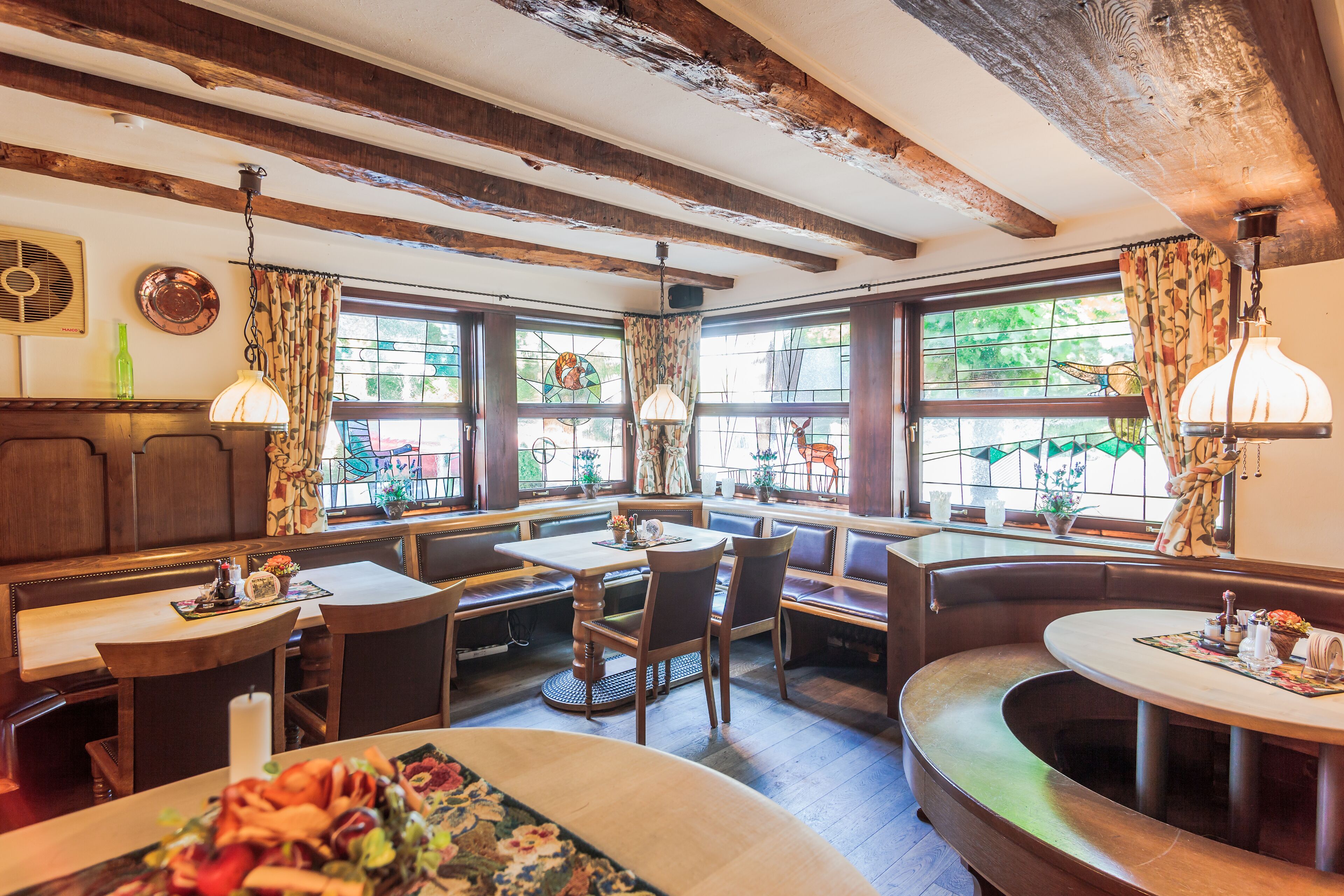 A cozy restaurant with wooden beams, large windows, and a variety of seating options including booths and tables.