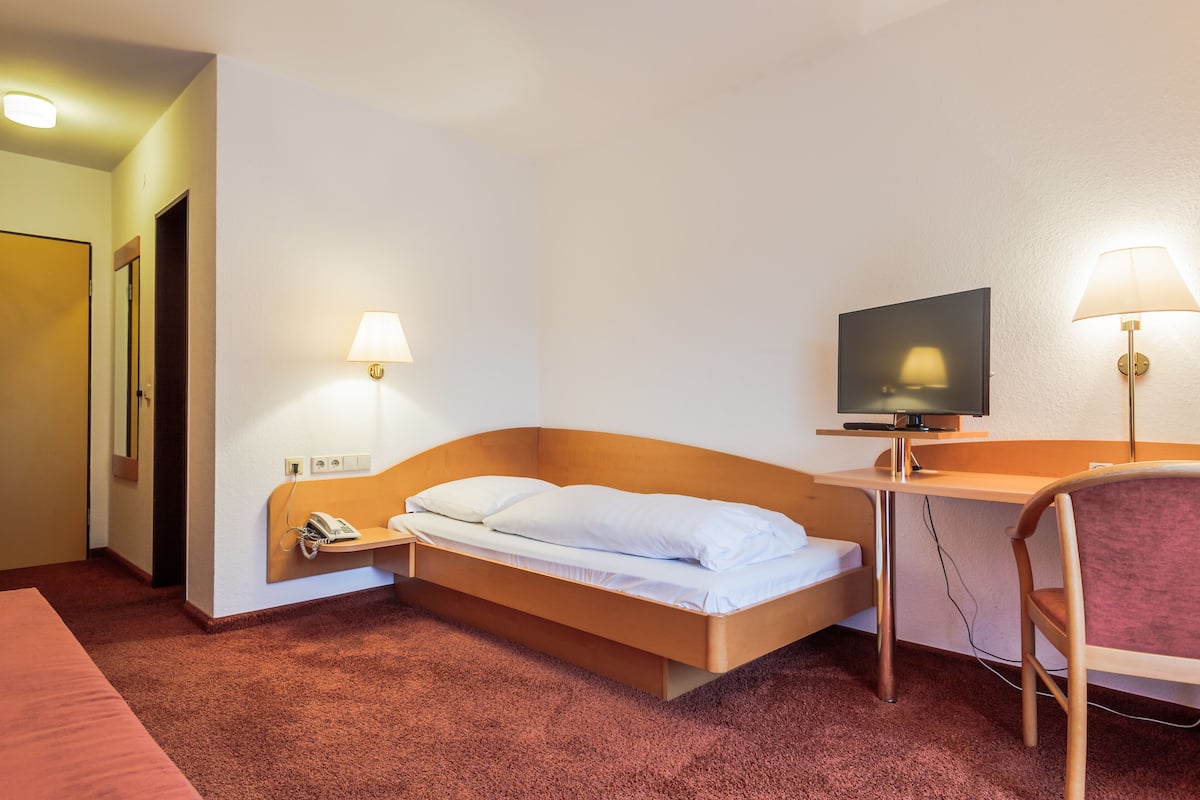Una habitación de hotel con cama, escritorio, silla, televisión y teléfono.