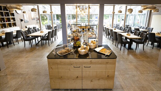 Een modern restaurant met een centraal eiland waarop etenswaren gepresenteerd staan, omringd door eettafels en stoelen.