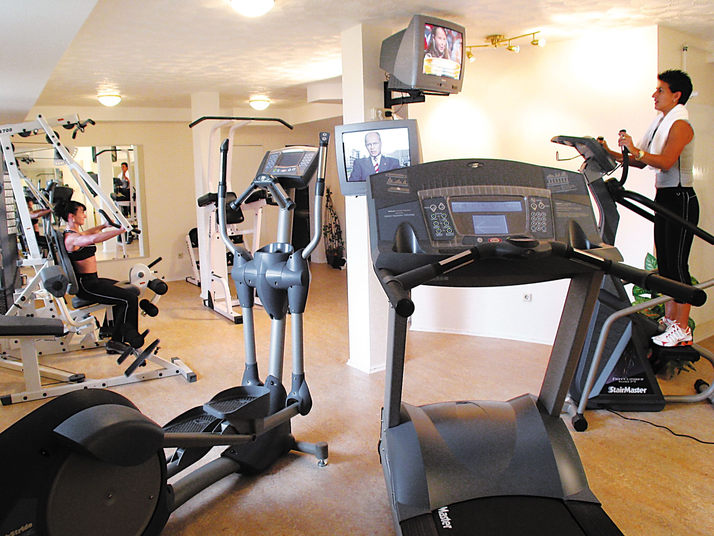 Une salle de sport équipée de tapis de course, d’appareils de musculation et d’un écran de télévision.