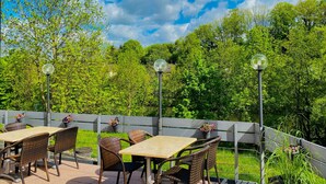 Een terras buiten met rieten meubilair en uitzicht op een weelderige tuin.