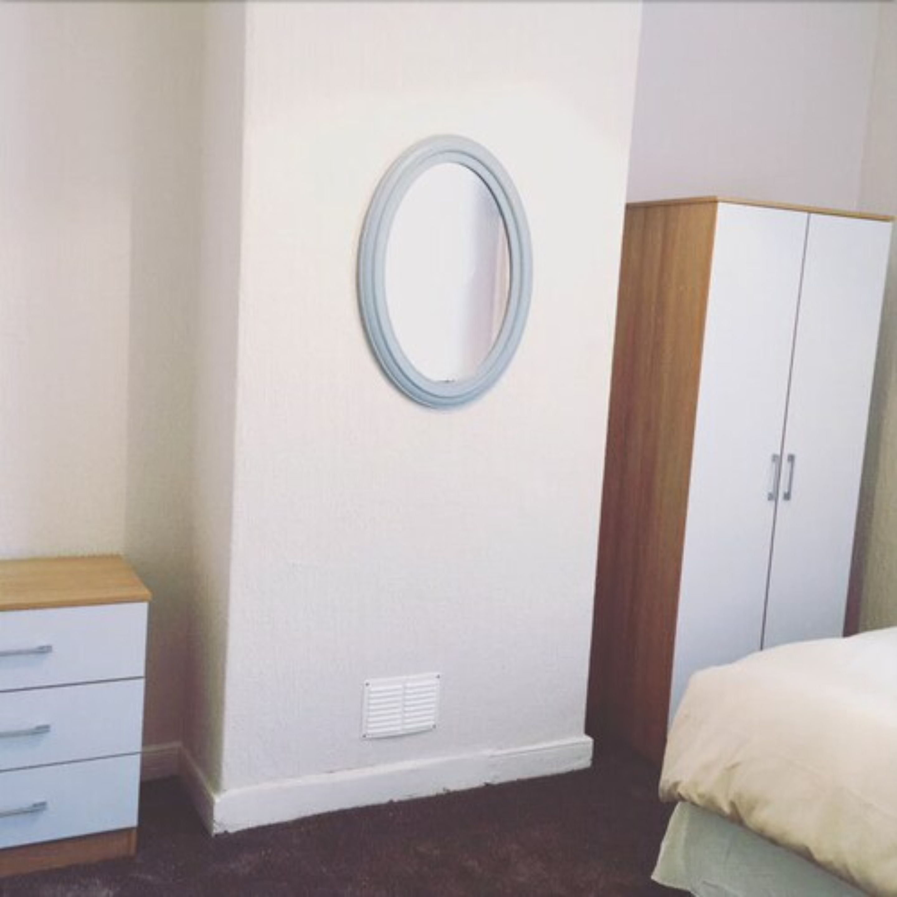 Quarto com cama, penteadeira, guarda-roupa e espelho fixado na parede.