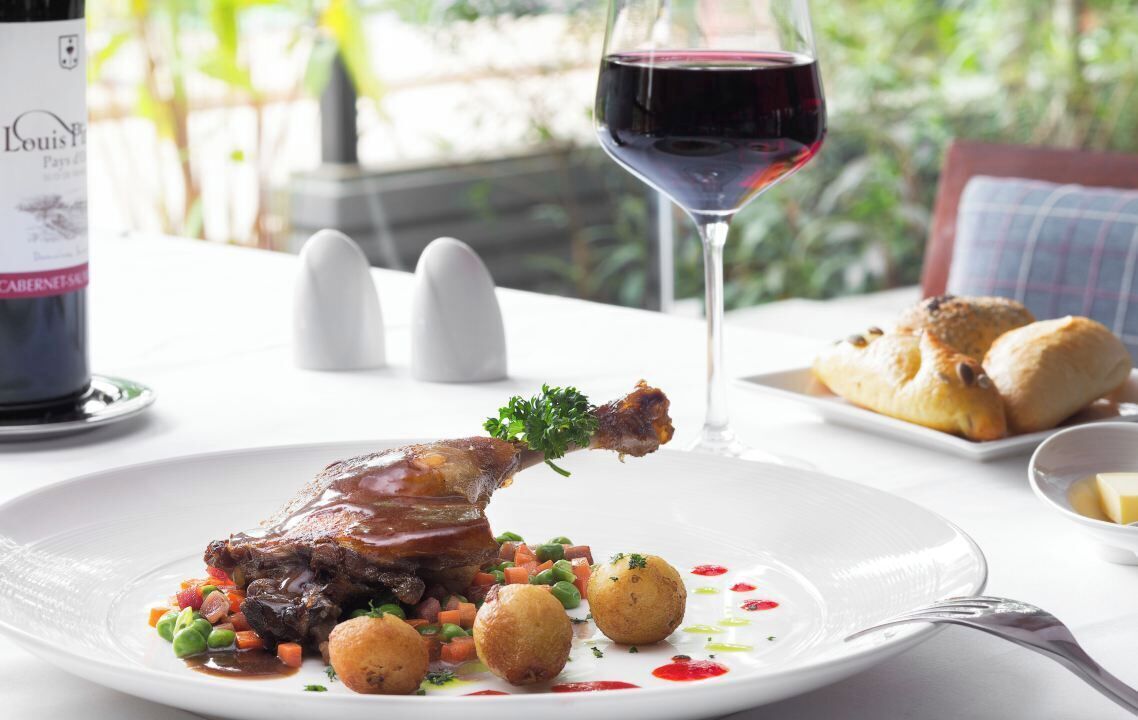 A dining table with a plate of food, a wine glass, and a bottle of wine.