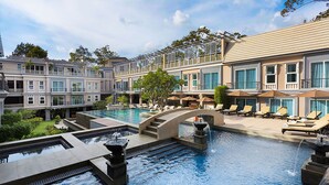 Ein Hotelpoolbereich mit einem zentralen Wasserspiel, Liegestühlen und einer Brücke.