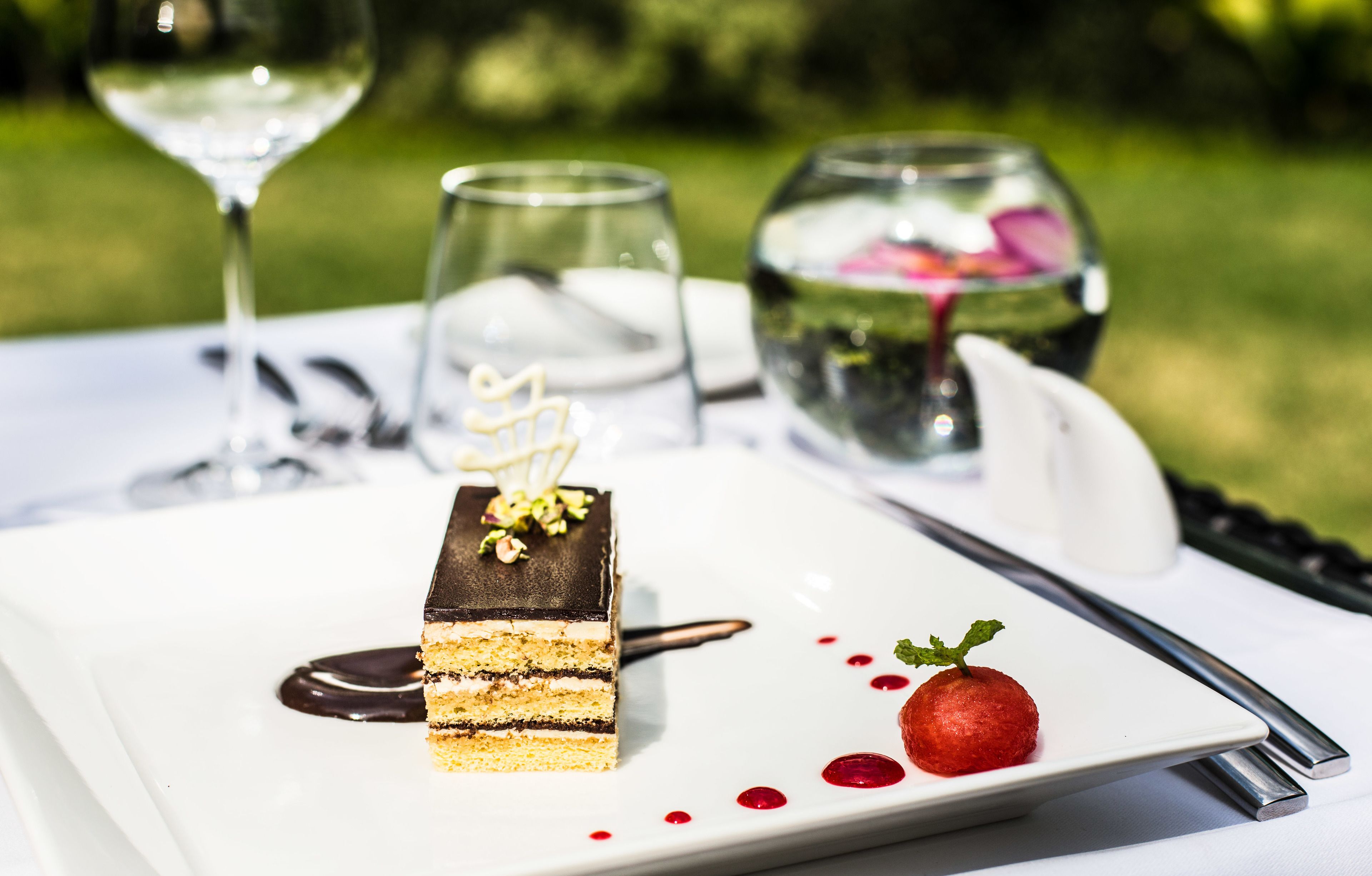 A dessert plate with a layered cake, a small fruit, and a glass of water.