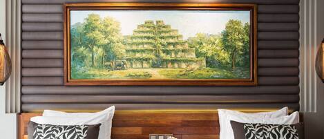 A hotel room with two beds, a wooden headboard, a painting of a temple, and a nightstand with a phone and flowers.