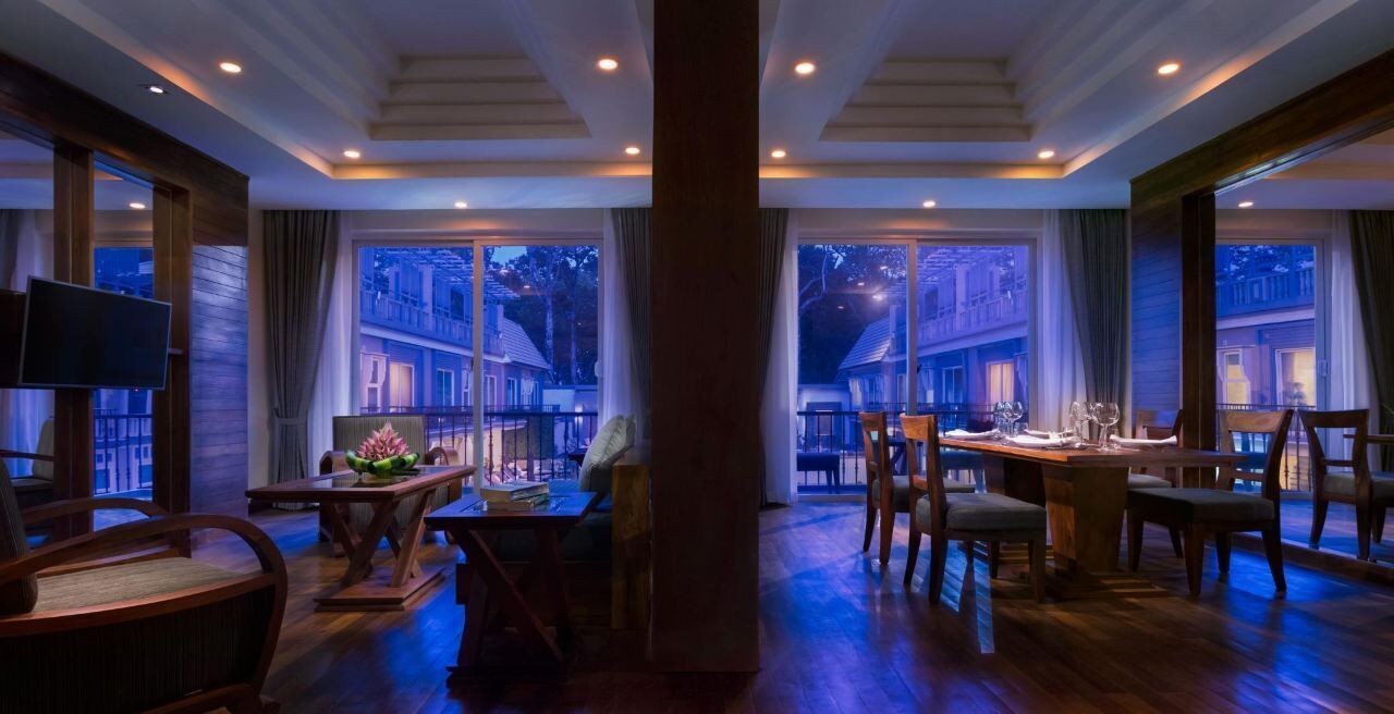 Un comedor amplio con una mesa grande y sillas, un televisor y vistas de la ciudad a través de grandes ventanales.