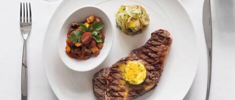A plate with a steak topped with butter, a side of vegetables, and a small bowl of sauce.