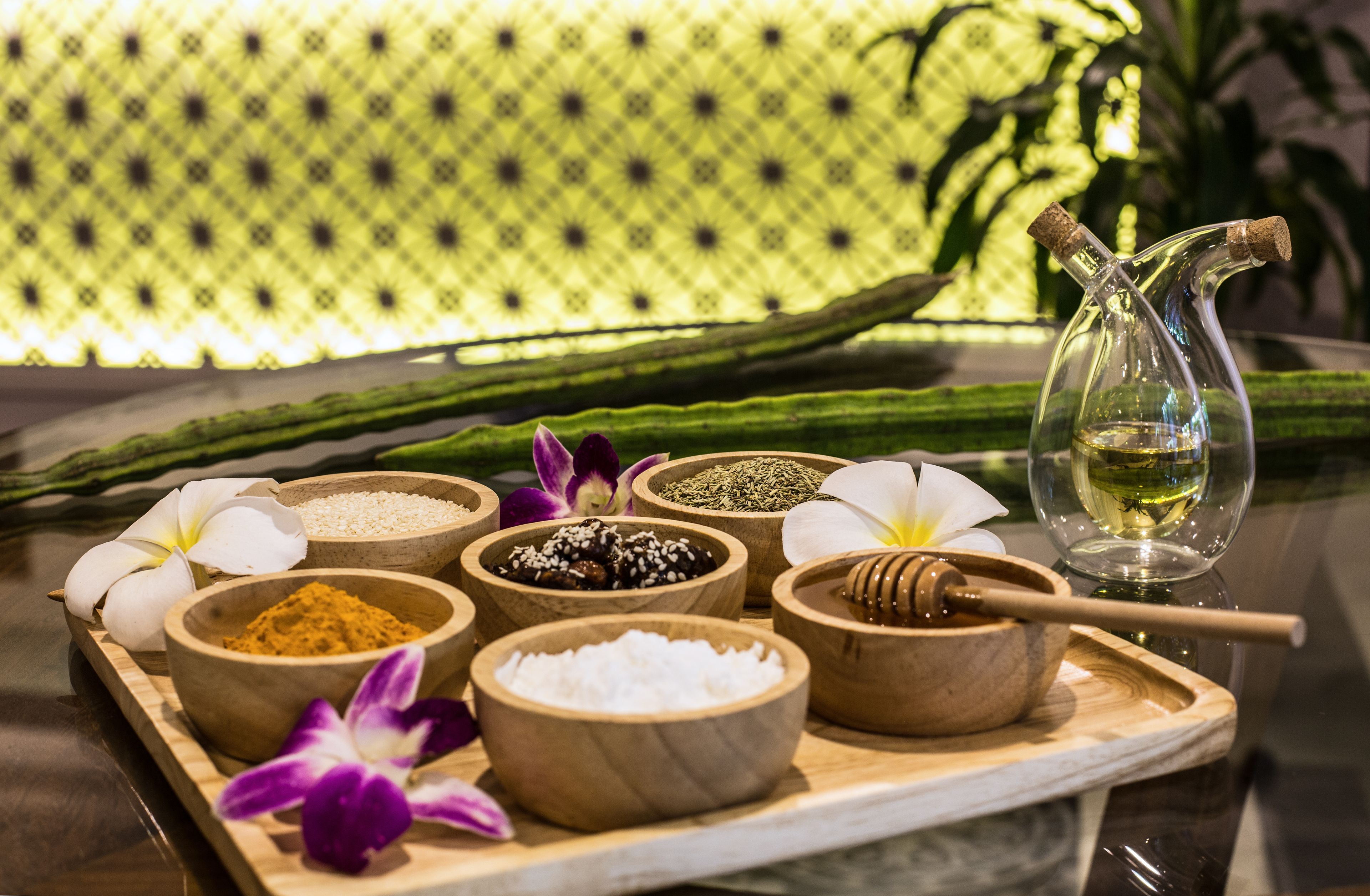 A wooden tray with various natural ingredients like spices, honey, and flowers, suggesting a spa or wellness setting.