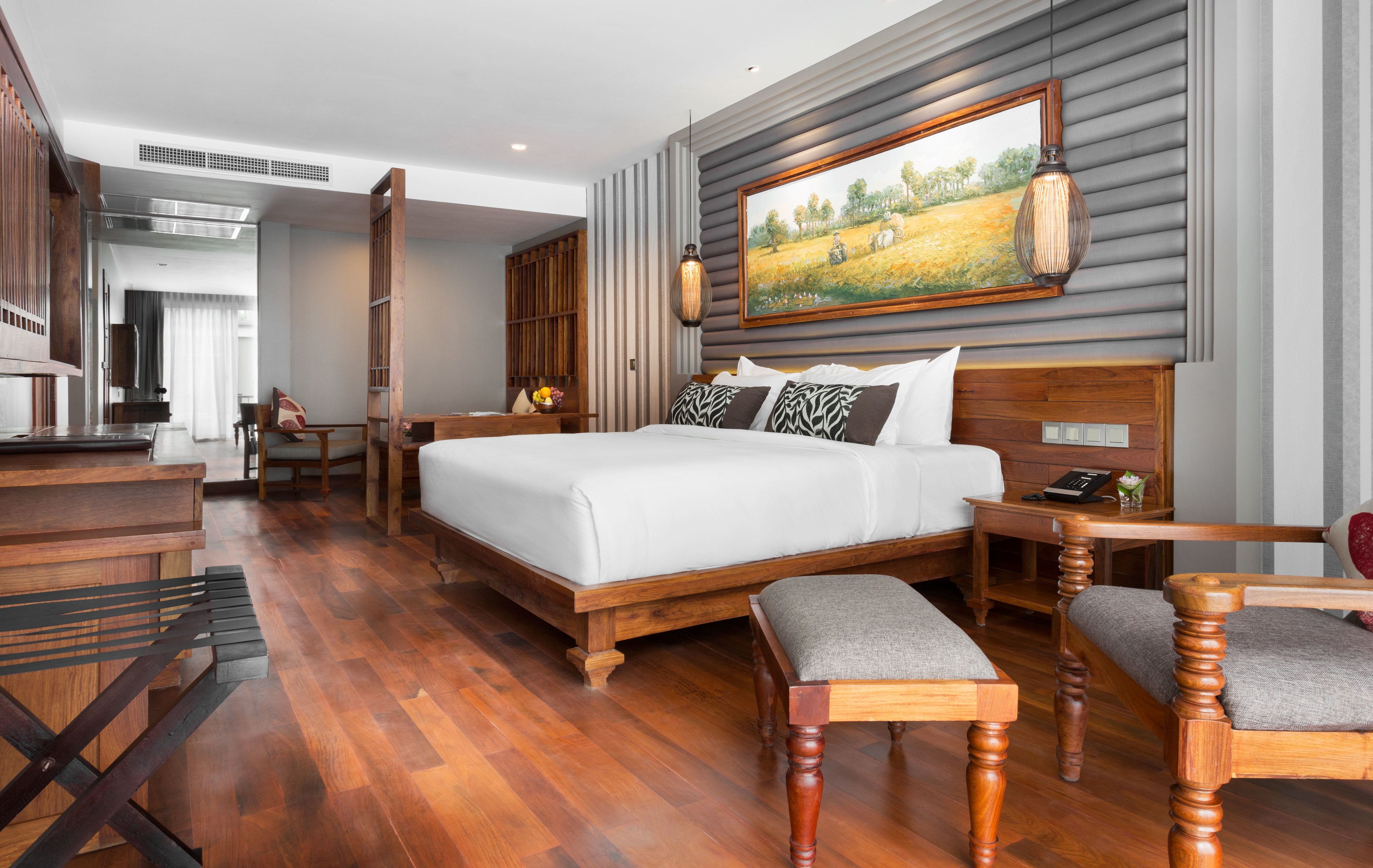 A modern hotel room with a large bed, wooden furniture, a painting on the wall, and a view of the outdoors.