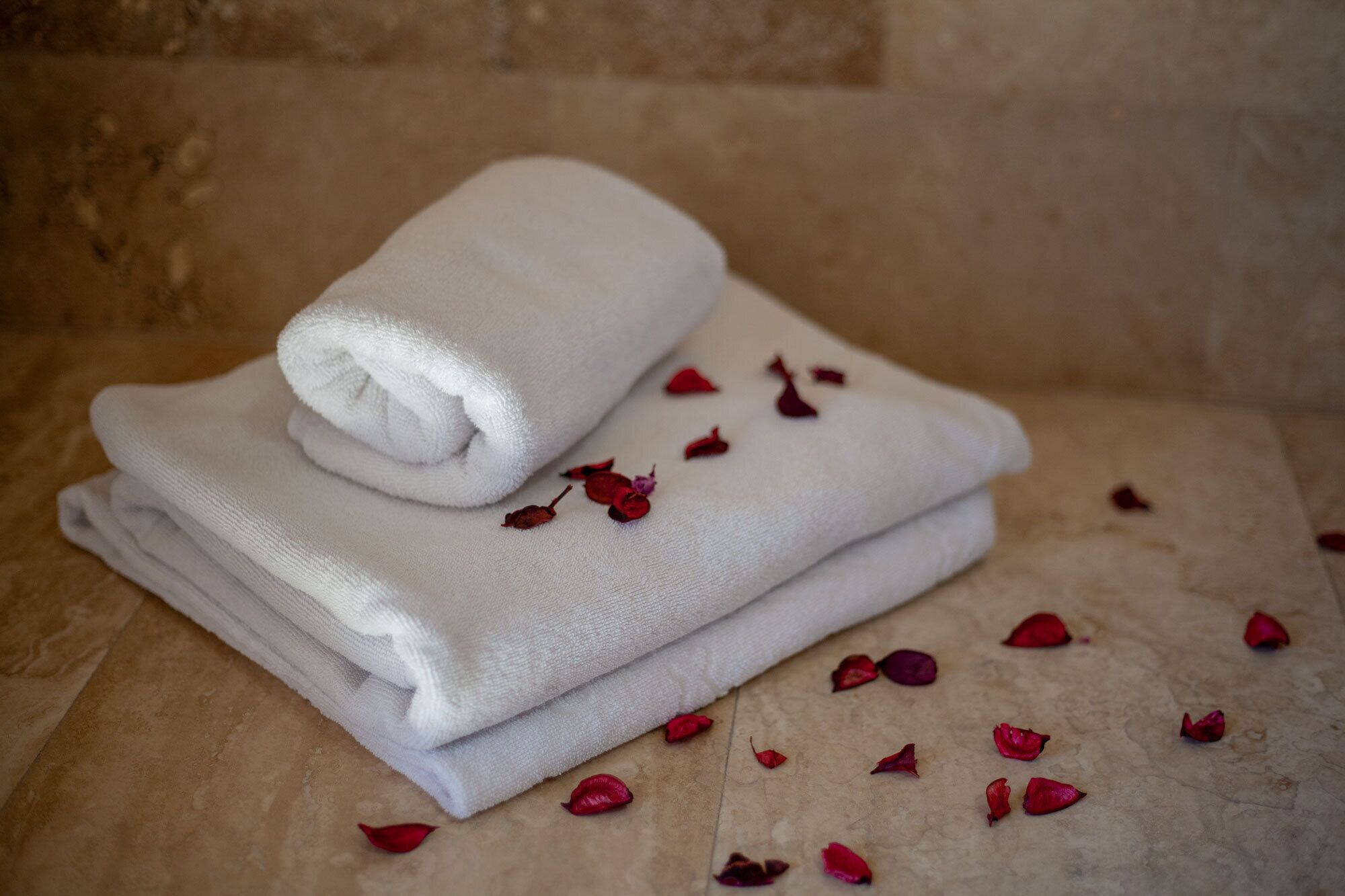A stack of white towels on a textured surface with scattered rose petals.