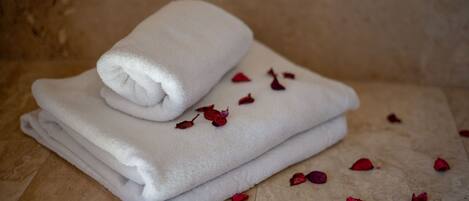 A stack of white towels on a textured surface with scattered rose petals.