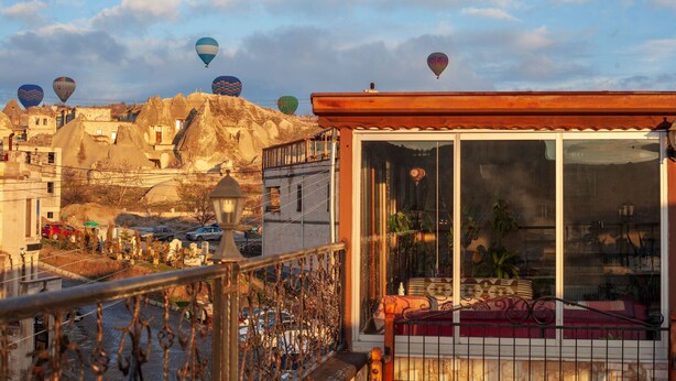 A hotel with a balcony overlooking a town with colorful hot air balloons in the background.