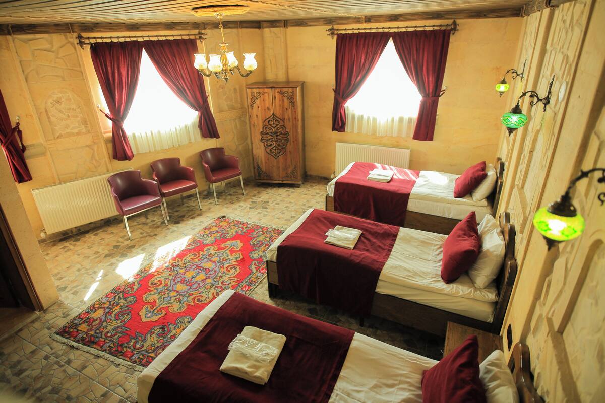 Habitación de hotel con dos camas individuales, un armario de madera, alfombra roja y un candelabro.