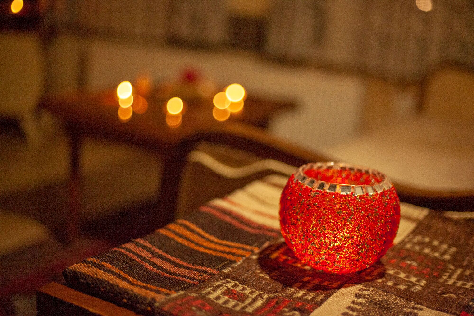 Una habitación acogedora con un tapete estampado, una mesita con una vela y un adorno rojo brillante.