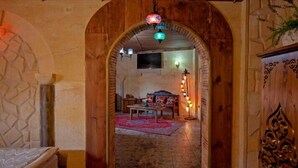 A narrow hallway with a wooden door leading to a room with a bed, a table, and a rug.