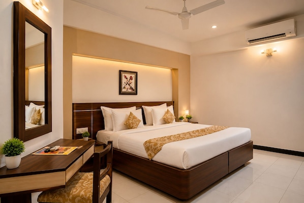 A hotel room with a large bed, a desk with a chair, a mirror, a ceiling fan, and an air conditioning unit.