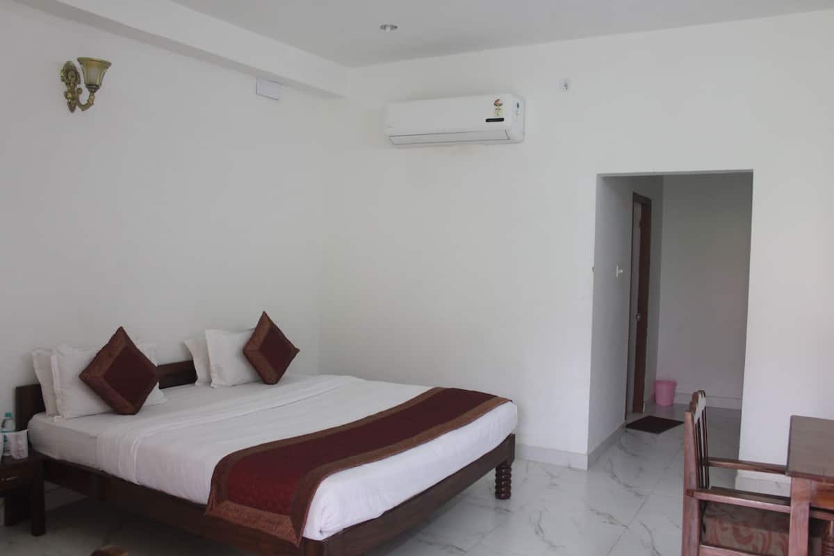A bedroom with a bed, a nightstand, a wooden chair, a wall-mounted air conditioner, and a door leading to another room.