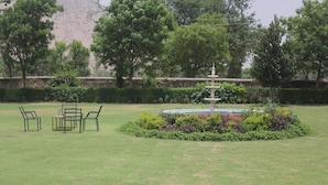 A park with a fountain, benches, and a stone wall in the background. - Sariska Tiger Camp Resort (Alwar)