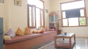 A room with a bench along the wall, a table, and a television. - Sariska Tiger Camp Resort (Alwar)