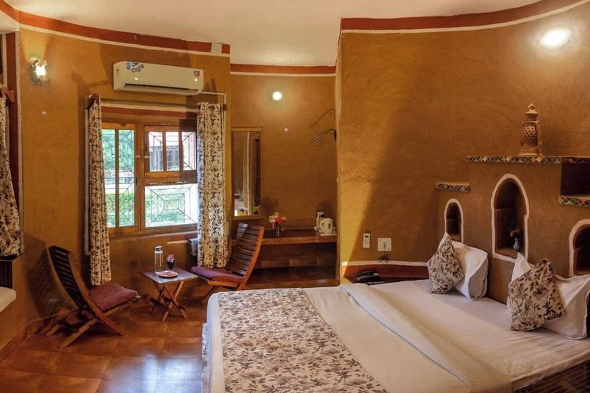 A bedroom with a bed, two chairs, a small table, a TV, and a window with curtains.