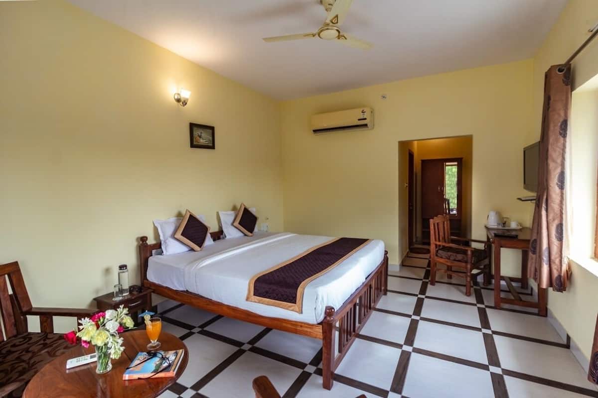 A hotel room with a bed, a desk, a chair, a table with flowers and a book, and a ceiling fan.