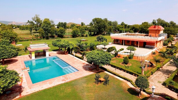 A large building with a swimming pool, surrounded by well-maintained lawns and trees. - Sariska Tiger Camp Resort (Alwar)