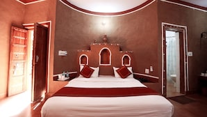 A bedroom with a large bed, two bedside tables, a nightstand, a wardrobe, and a bathroom door. - Sariska Tiger Camp Resort (Alwar)